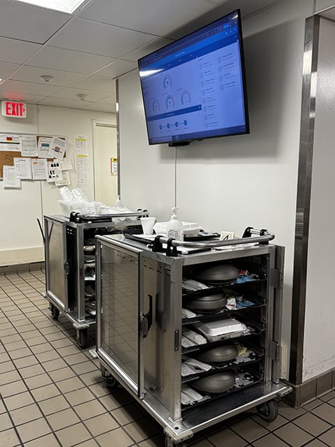 A photo of Tray InMotion Elite dashboard metrics displayed on a TV in Carle Foundation Hospital's kitchen