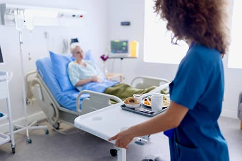 Image of a caregiver delivering a hospital meal through patient room service
