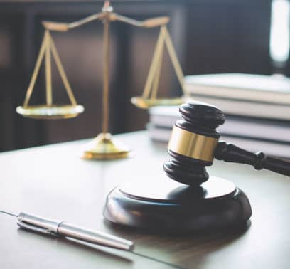 A desk with a gavel and block, a pen, a stack of books, and scales of justice.