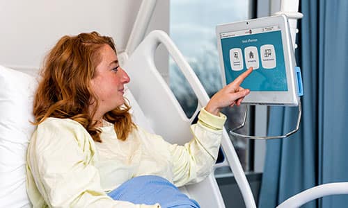 A graphic of a patient in bed using touchscreen menu ordering technology.