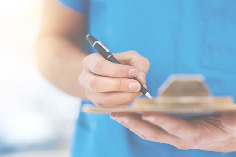 A nurse in blue scrubs writes on a clipboard with a black pen because her department doesn’t have a mobile floor stock solution.