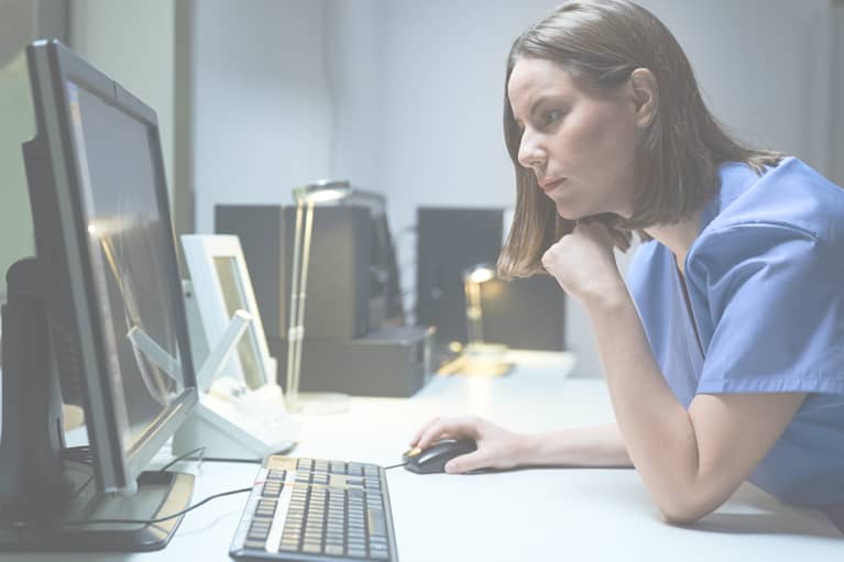 A profile shot of a nurse working on a computer in a hospital office, doing floor stock inventory management.