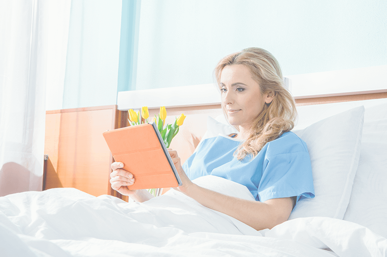A hospital patient using a tablet in her bed. There are yellow flowers in the background.