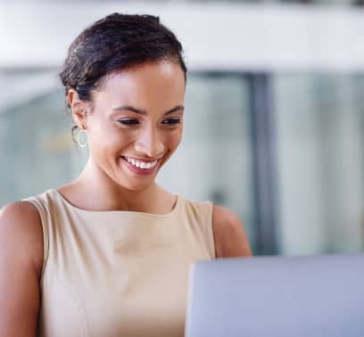 A woman grins as she looks down at a computer screen.