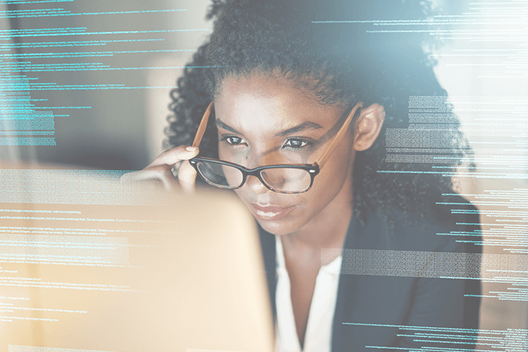 A professionally dressed woman tips down her glasses as she observes a computer screen. The image is overlaid with small, technical text.